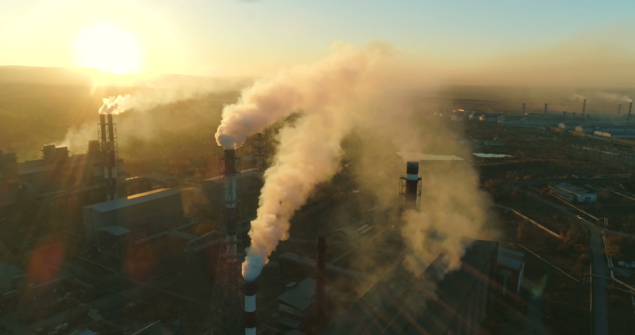 Air pollution. clouds of smoke coming from the chimneys of the plant with beautiful golden yellow lighting of setting sun. Drone flying over smoking smokestacks of a steel factory. Royalty-Free Stock Footage #1029987017
