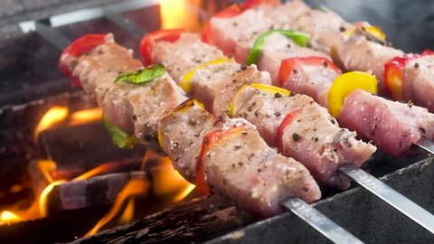 Pork meat and bell pepper skewered on skewers. sprinkled with spices and pepper. Is preparing on hot coals. flames and smoke, juicy crust, barbecue outdoors. Cooking on an open fire. Slow motion
