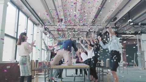 Manager start to dance on the table, sings into a megaphone, accelerates and slide on lap. Colleagues blow up flappers with confetti. Employees celebrate success. Corporate party business team