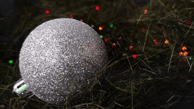 Christmas background, seamless looped video: close-up of silver shiny ball (Christmas decoration) on dark background with colourful flashing lights of electric garland.