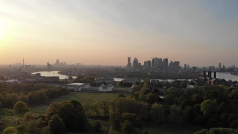 Aerial viewing forward towards London skyline and Canary Wharf as seen from above the Greenwich Park at sunset