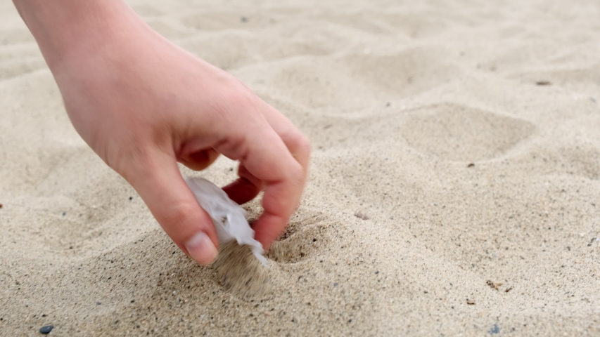 Plastic waste piece on sand beach being picked up, closing in shot