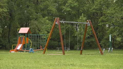 Empty playground after rain. Swing got wet in raindrops. Summer or spring rainy day. No people. No children.