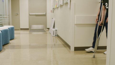 Tracking shot of father and smiling daughter walking with crutches talking to nurse in hospital / Salt Lake City, Utah, United States