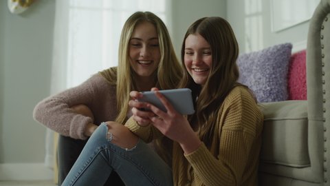 Girls sitting on livingroom floor watching video on cell phone and laughing / Cedar Hills, Utah, United States