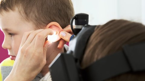 Woman doctor otorhinolaryngologist examines the ear of a baby boy, close-up