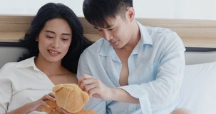 Close up scene video of Asian couple lying on bed, they playing with teddy bear, concept for free time in bedroom.
