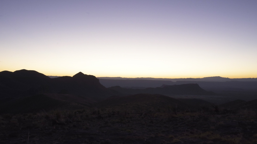 Dolly shot to the left of golden gloving sunset, over dark, moody grassland in mountains