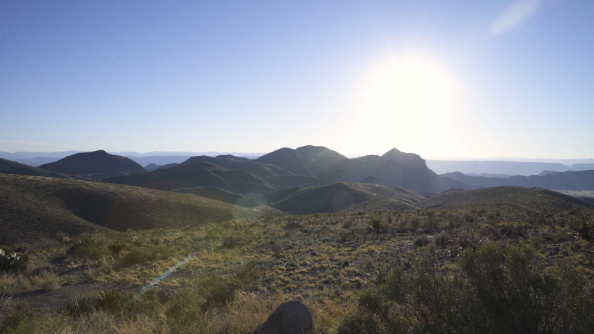 Push in shot over dry highlands landscape, shot against the sun, with lens flare