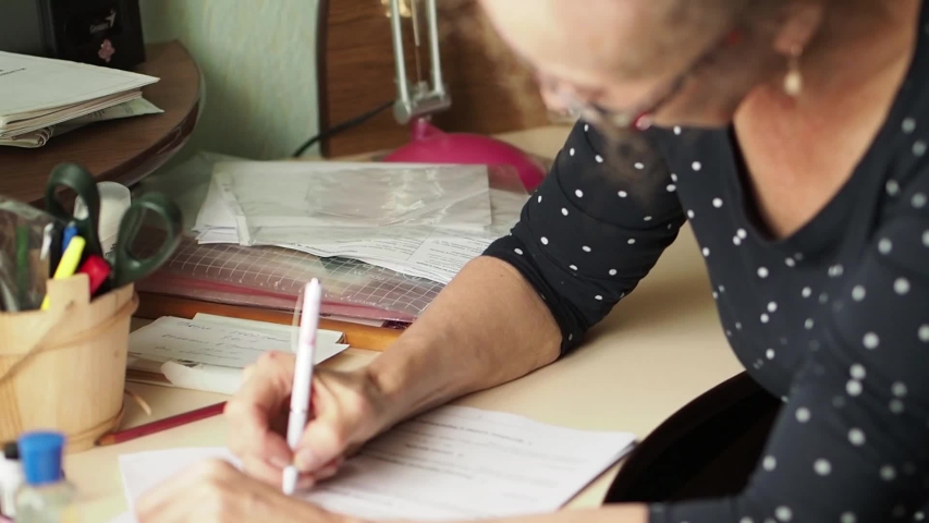 An elderly lady reads the document and makes her notes in it. Woman during operation. Close-up head tilt curly blond natural hair. 
