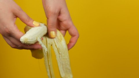 Female hand with yellow manicure peels the skin a ripe banana fruit on a yellow background