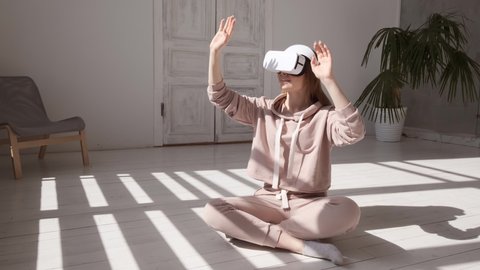 Beautiful young girl wearing virtual reality headset. Augmented Reality. Happy cute woman touch something using modern 3D vr glasses indoors. Woman playing using VR glasses on a sunny day. Shot on 4K
