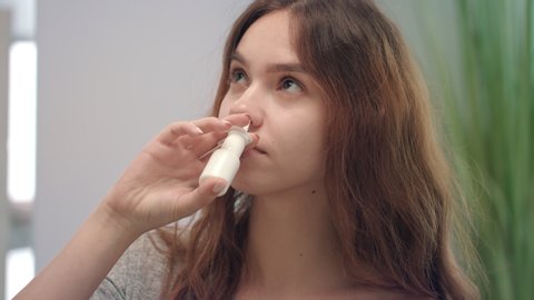 Young woman feeling blocked nose while allergy and spraying nasal spray. Portrait ill woman using nose spray for treatment respiratory disease. Health care and therapy concept
