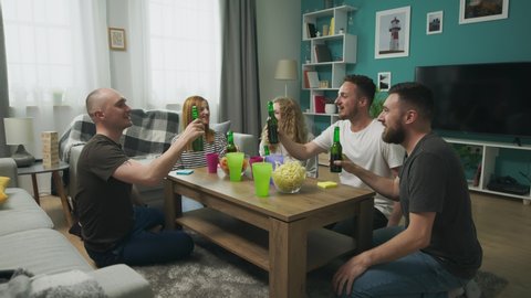 Cheerful company of friends clink glasses in a cozy living room