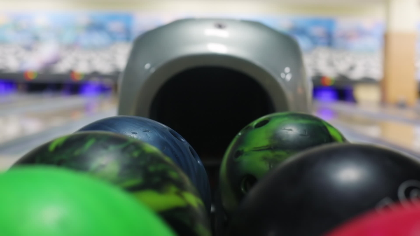 Close-up of young men taking bowling balls from the rack. Competitive cheerful friends playing bowling together in the club.