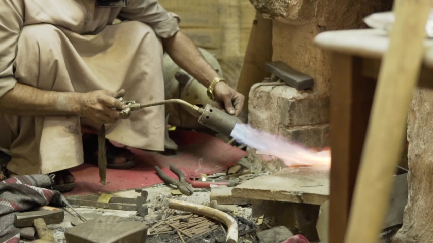 Man is heating up the metal. Slow moton.