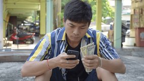 male man wearing colorful pattern-shirt holding with a left and right hand holding black smartphone, American money - US Dollars (USD),holding dollar banknotes banking and people concept