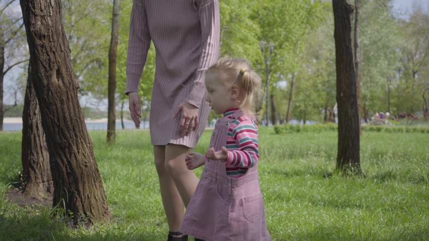 Cute little girl playing in the park with her mother, pointing with tiny finger away. Woman explaining her kid how is ther world. Carefree child resting outdoors with parent. Active healthy lifestyle