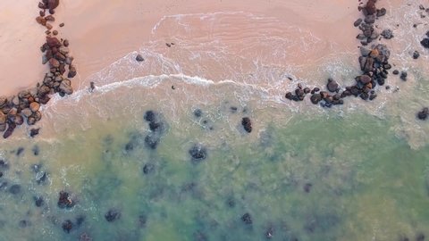 Aerial view of sand beach and clear ocean. Top view sea waves and stones HD video, flying over tropical sandy beach and waves, there is sunrise. It is tropical paradise.