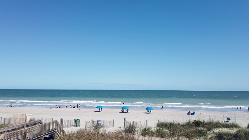 People walking on the beach and sitting under umbrellas in chairs under a clear blue sky at Myrtle Beach South Carolina 