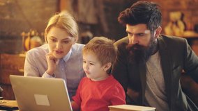 Beautiful young parents and their child boy are using a laptop at home. Young family with son using laptop together looking at screen. Couple with kid shopping or watching video online. Happy family