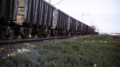 A long logistics train moves iron ore in carriages along railway tracks that pass the camera into the distance.