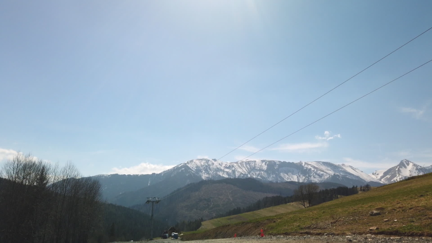 Timelapse of offseason ski lift as people walk down slope in Vysoke Tatry, Slovakia. High Tatras mountains seen in distance.