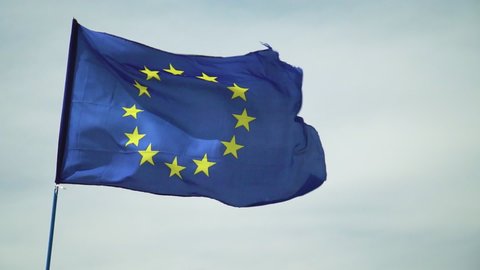 Slow motion EU European Union flag, Blue with gold circle of stars floating &ing slow motion in the wind against off white cloudy sky.