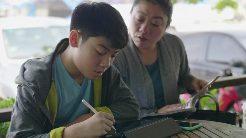 Asian boy is playing tablet computer. And talk to his mother with smile face.