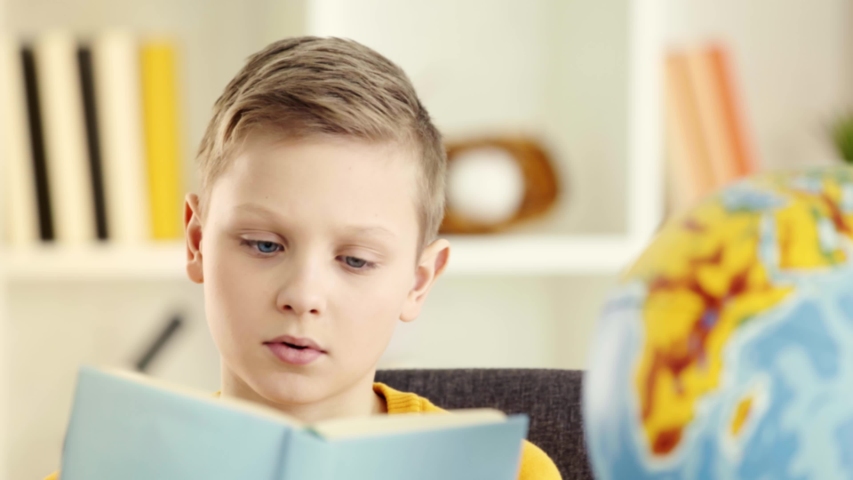 Selective focus of cute schoolboy reading, putting book on head and sighing at home | Shutterstock HD Video #1030104206