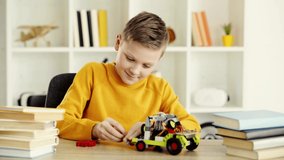 happy kid playing with electric car made of building blocks near books on table at home