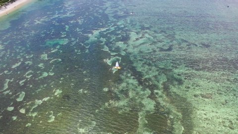 Aerial zoom into a yellow sailing boat on the clear blue tropical water near Flic en Flac, Mauritius