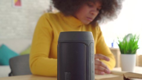 african woman with an afro hairstyle enjoys voice assistant reading a book at the table close up