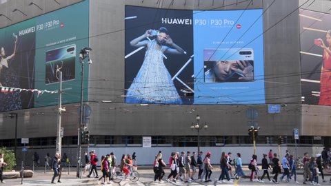 Milan, Italy - 24 May 2019: People walk past a giant billboard promoting the new Huawei P30 and P30 Pro Android smartphones.