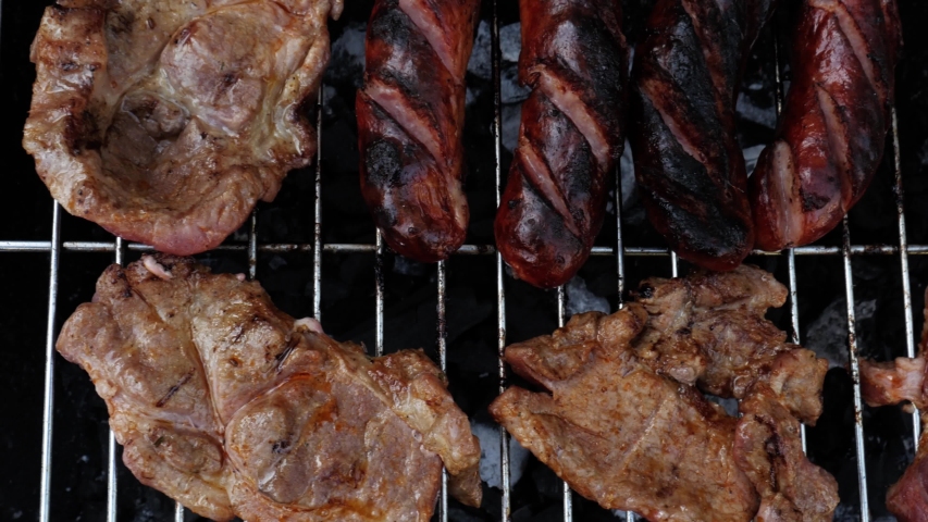 Top view dolly shot to right over a barbecue, tasty sausages and meat on the grill