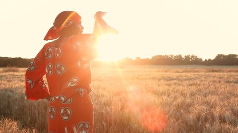 African woman farmer in traditional clothes standing in a farm field of crops in Africa at sunset or sunrise