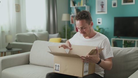 Young man in his living room opening cardboard box package