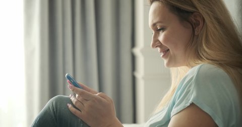 Adult blonde woman using mobile phone, at home.