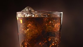 Cola with ice cubes close-up. Cola with Ice and bubbles in glass. Soda closeup. Food and drink background. Rotated glass of Cola fizzy drink over brown background. Slow motion 4K UHD video footage