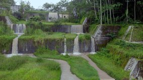 Cinematic aerial footage drone flying slow sideway down motion view of waterfall cascade dam step down with green trees around and water flowing in small river