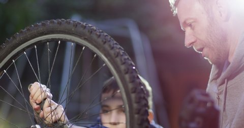 4K Teen boy learning from his dad, doing bike repairs out in the yard. Slow motion.