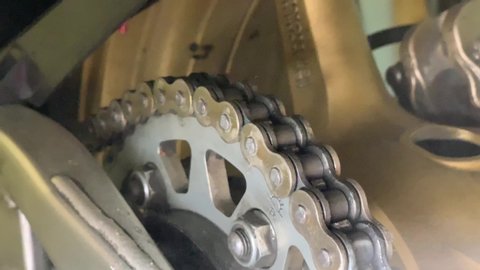 Oiling a motorcycle chain in a workshop. Woman is lubricating moto chain with lube. Closeup of spraying motorbike chain with oil lubricant.