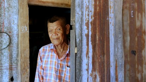 Elderly farmers, Asian poor people who living in an old house with zinc roofs and walls. Dilapidated, is opening the door