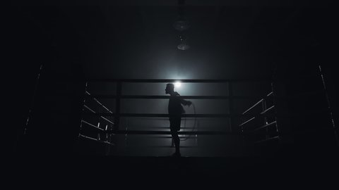 Male boxer wrapped in bandage jumping on the skipping rope in the dark ring. Slow motion. Silhouette. Boxing concept.