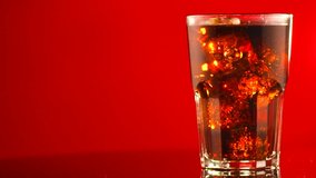 Cola with ice cubes close-up. Cola drink with Ice and bubbles rotated in glass on red background. Coke Soda closeup. Food border. Glass of Cola fizzy drink. Slow motion 4K UHD video footage