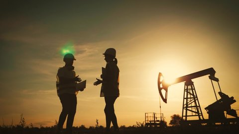 Silhouette two engineers shaking hands on the background a oil pump at sunset. Industrial, oil and gas concept.