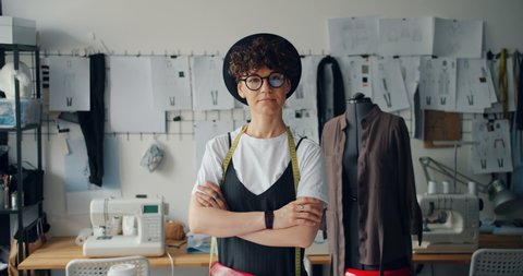 Portrait of independent young woman clothes designer standing in studio with arms crossed looking at camera. Successful youth and small business concept.