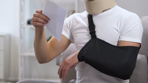 Shocked man in arm sling and cervical collar looking at medical bill, expanses