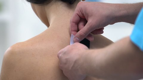 Doctor applying Y-shaped tapes on female upper back, reduce muscle tension