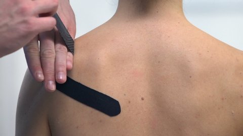 Therapist applying Y-shaped tapes on female shoulder, sport trauma muscle pain